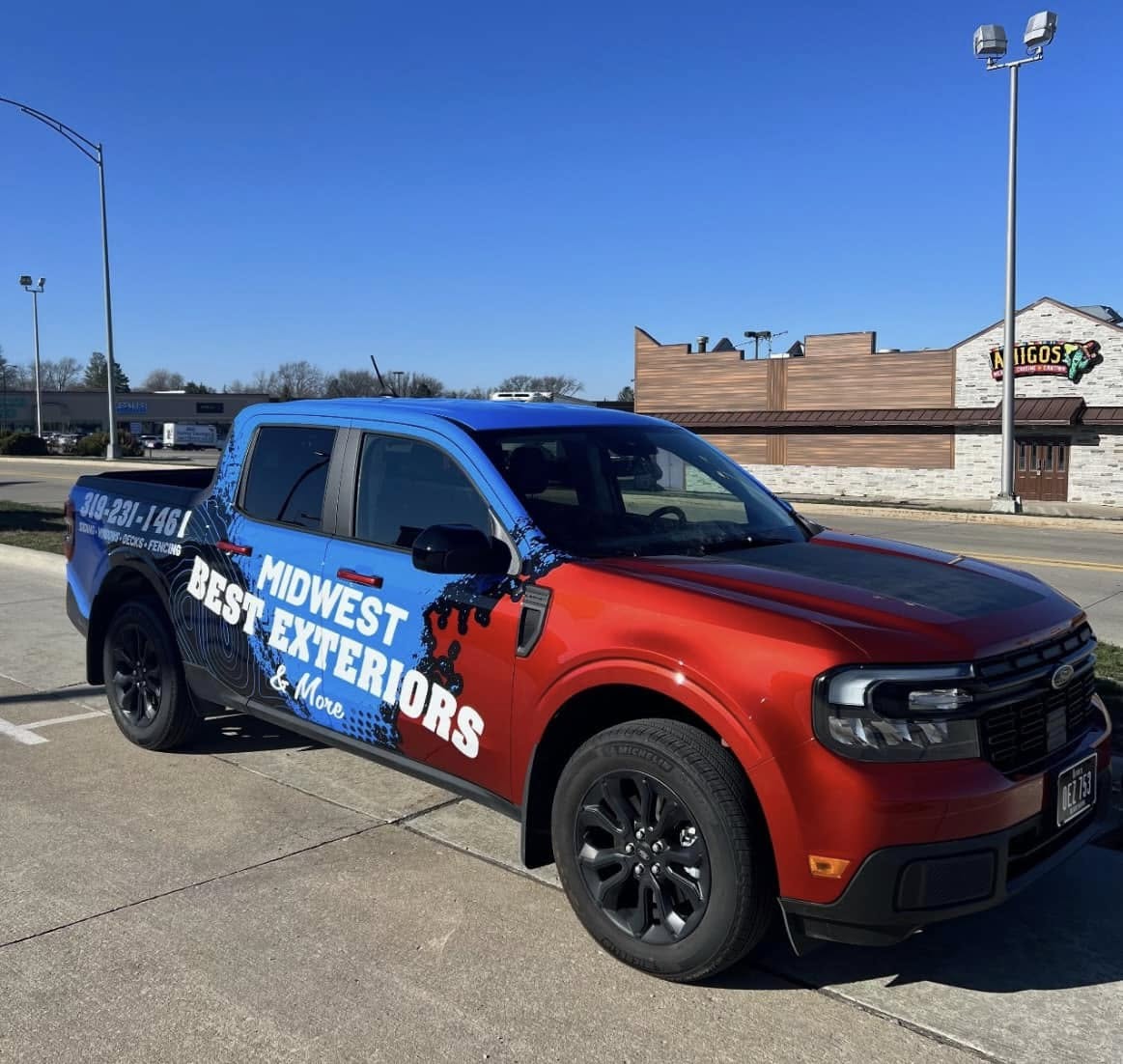 472817006_122213340158032934_2543134550192102297_n Pickup truck with red and blue wrap displaying "Midwest Best Exteriors & More" parked on a street, advertising roofing, siding, windows, decks, and fencing services in Eastern Iowa.
