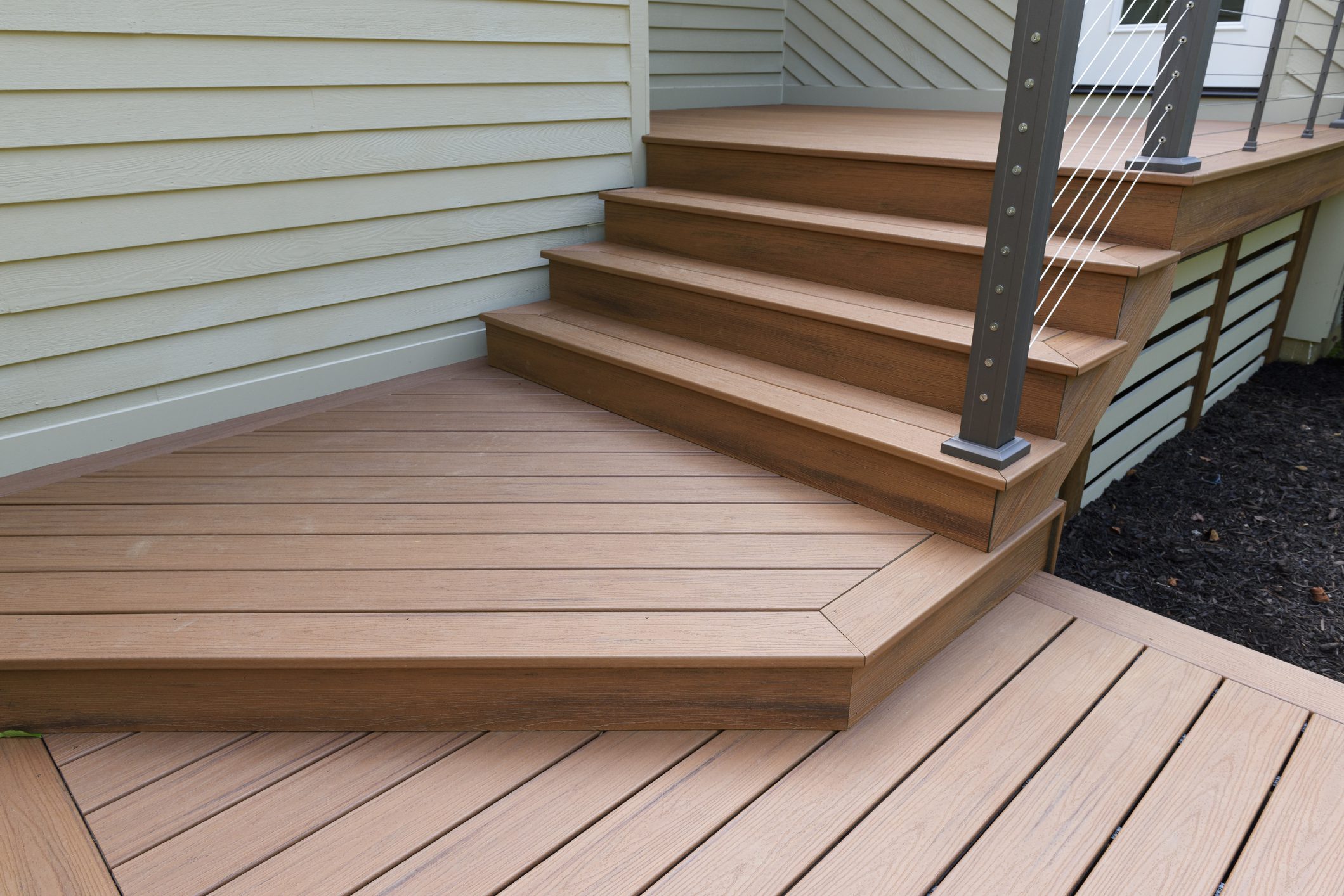 Composite wood deck and stairs with cable railing installed next to beige house siding, showcasing durable and stylish exterior home improvement by Midwest Best Exteriors.