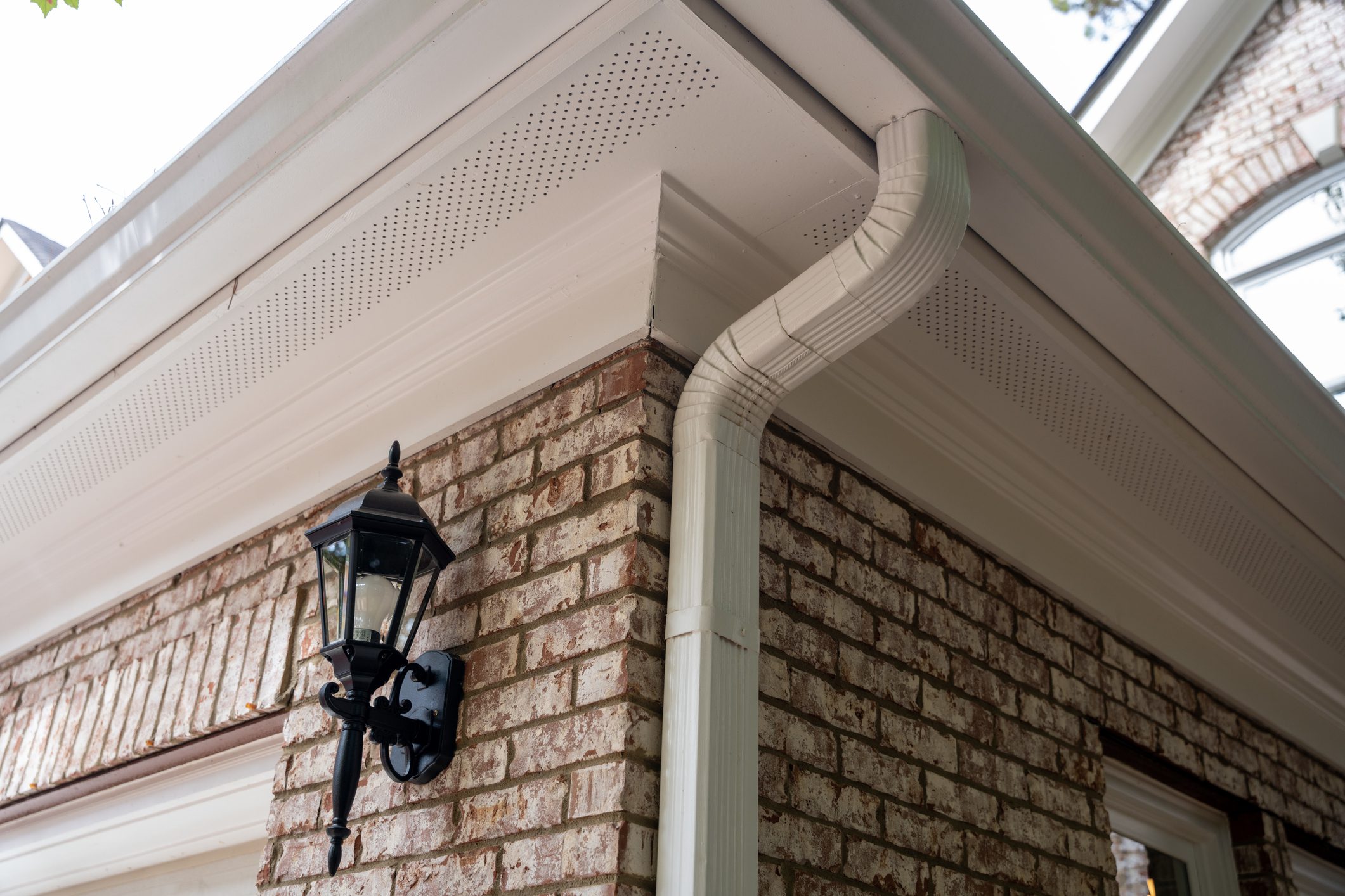 close-up of white seamless gutters and downspout installed on a brick home exterior with a black outdoor wall lantern, showcasing professional exterior home improvement services in Cedar Falls, Eastern Iowa by Midwest Best Exteriors