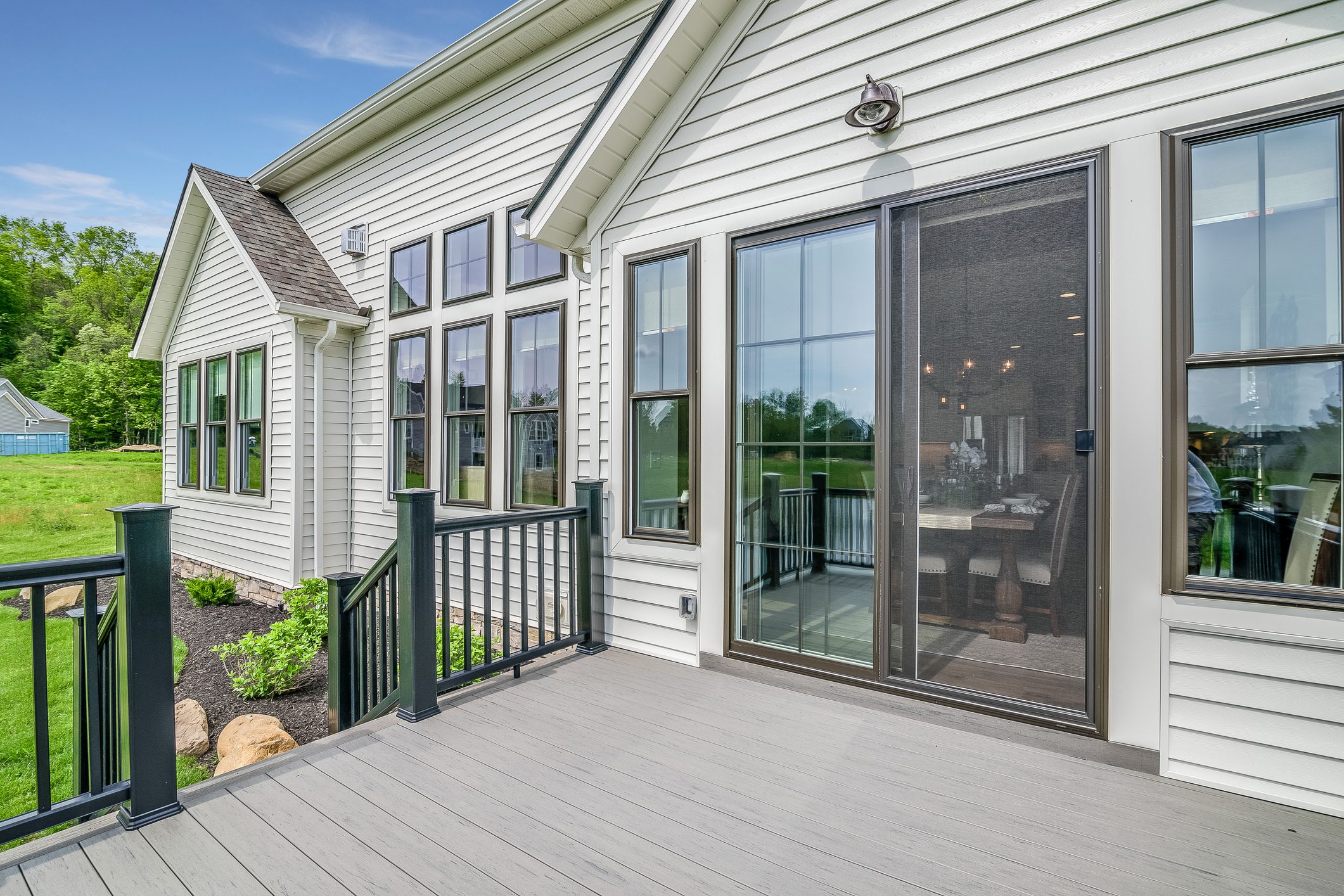 Modern home exterior featuring white siding, large energy-efficient windows, sliding glass door opening to a spacious deck with black railing, showcasing expert craftsmanship in home improvement and exterior upgrades.
